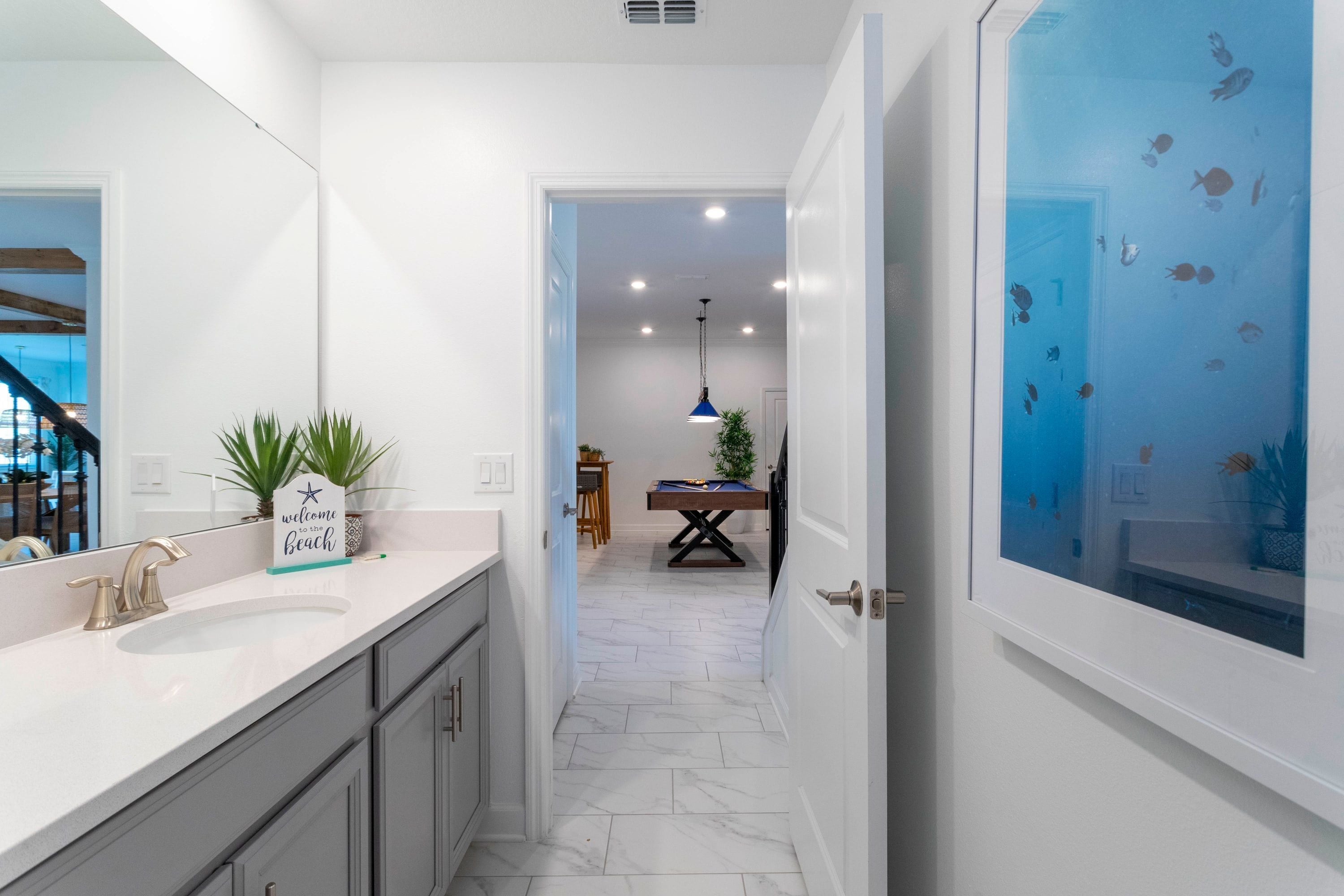 A modern bathroom with a white sink, a blue pendant light, and a door with a fish decal.