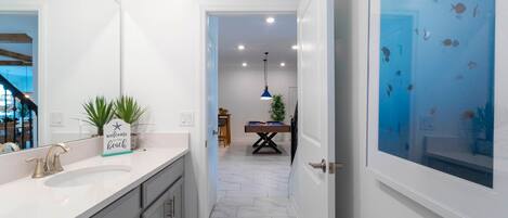 A modern bathroom with a white sink, a blue pendant light, and a door with a fish decal.