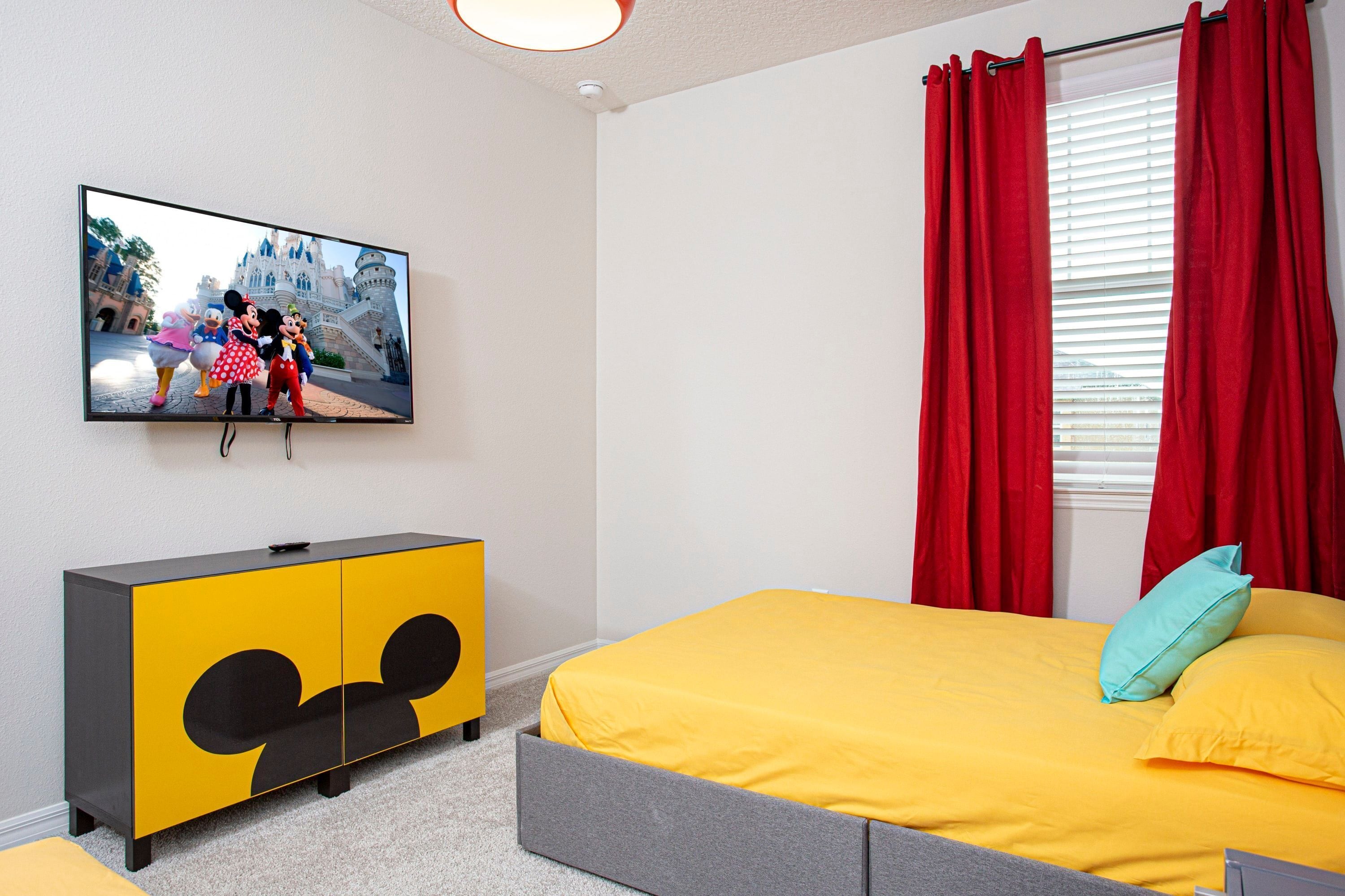 Een slaapkamer met een bed, een televisie aan de muur en een kast met een Mickey Mouse thema.