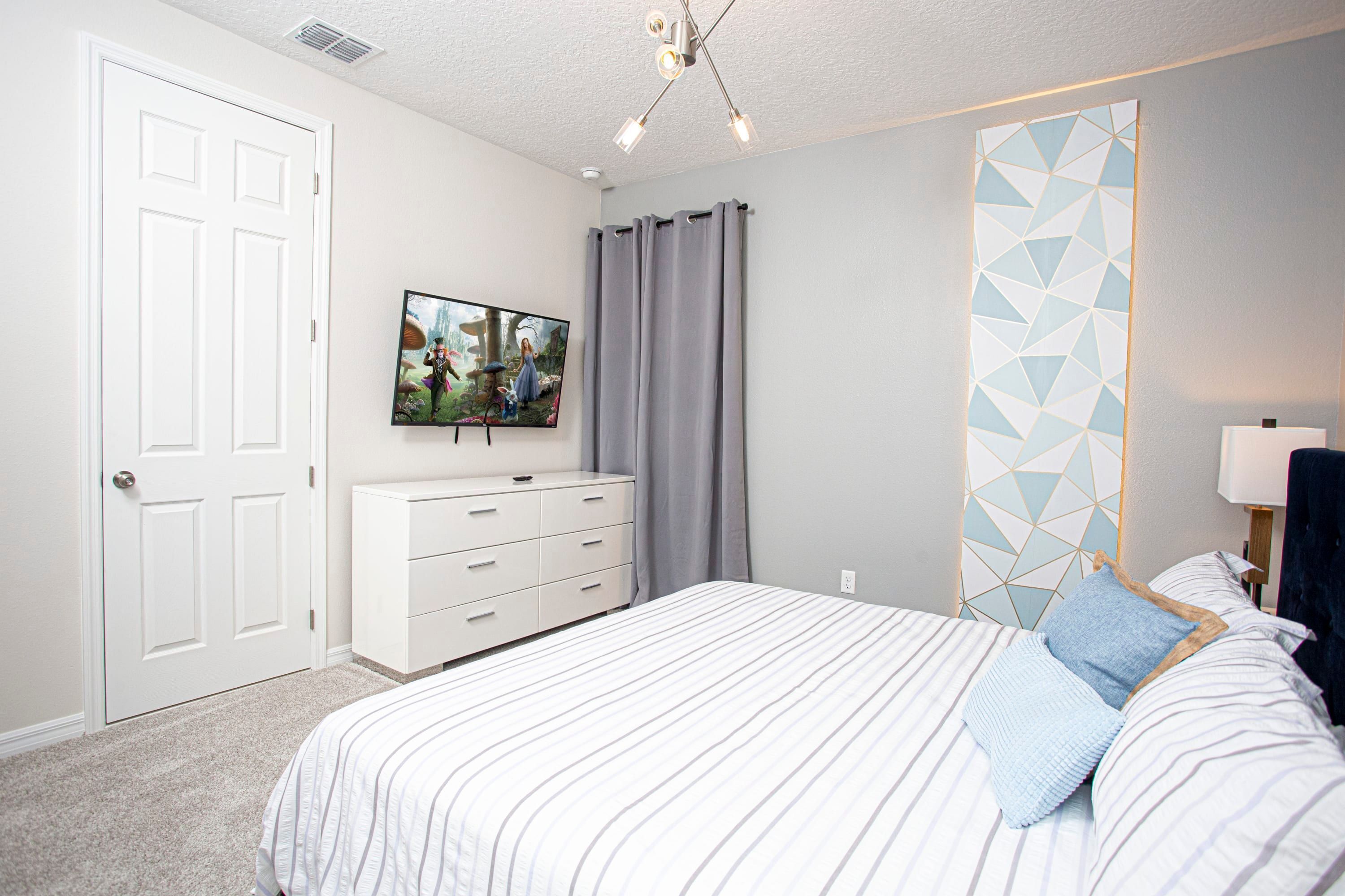 A bedroom with a bed, a dresser, a TV, and a geometric-patterned wall.