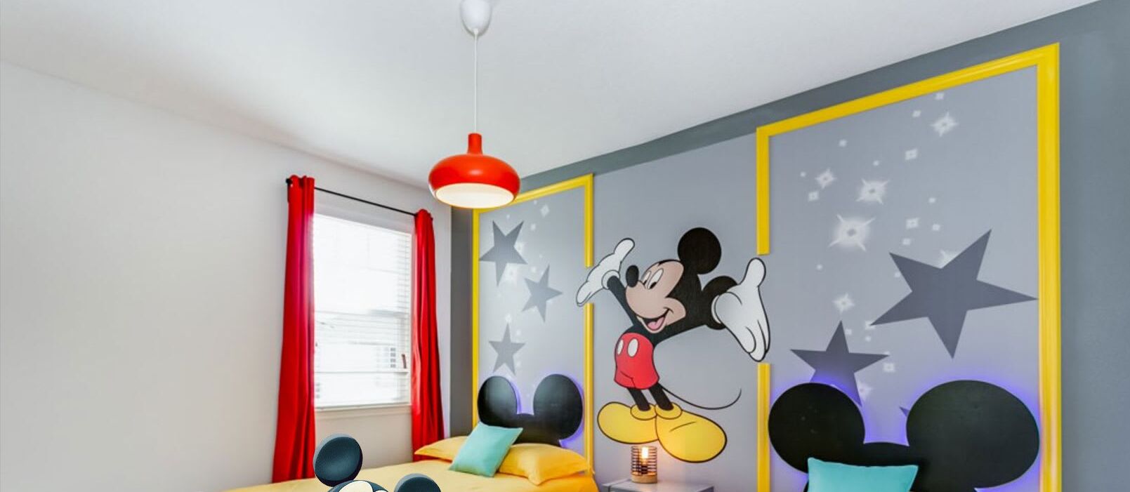 A child's bedroom with a Mickey Mouse mural, a bed with colorful pillows, and a red pendant light.
