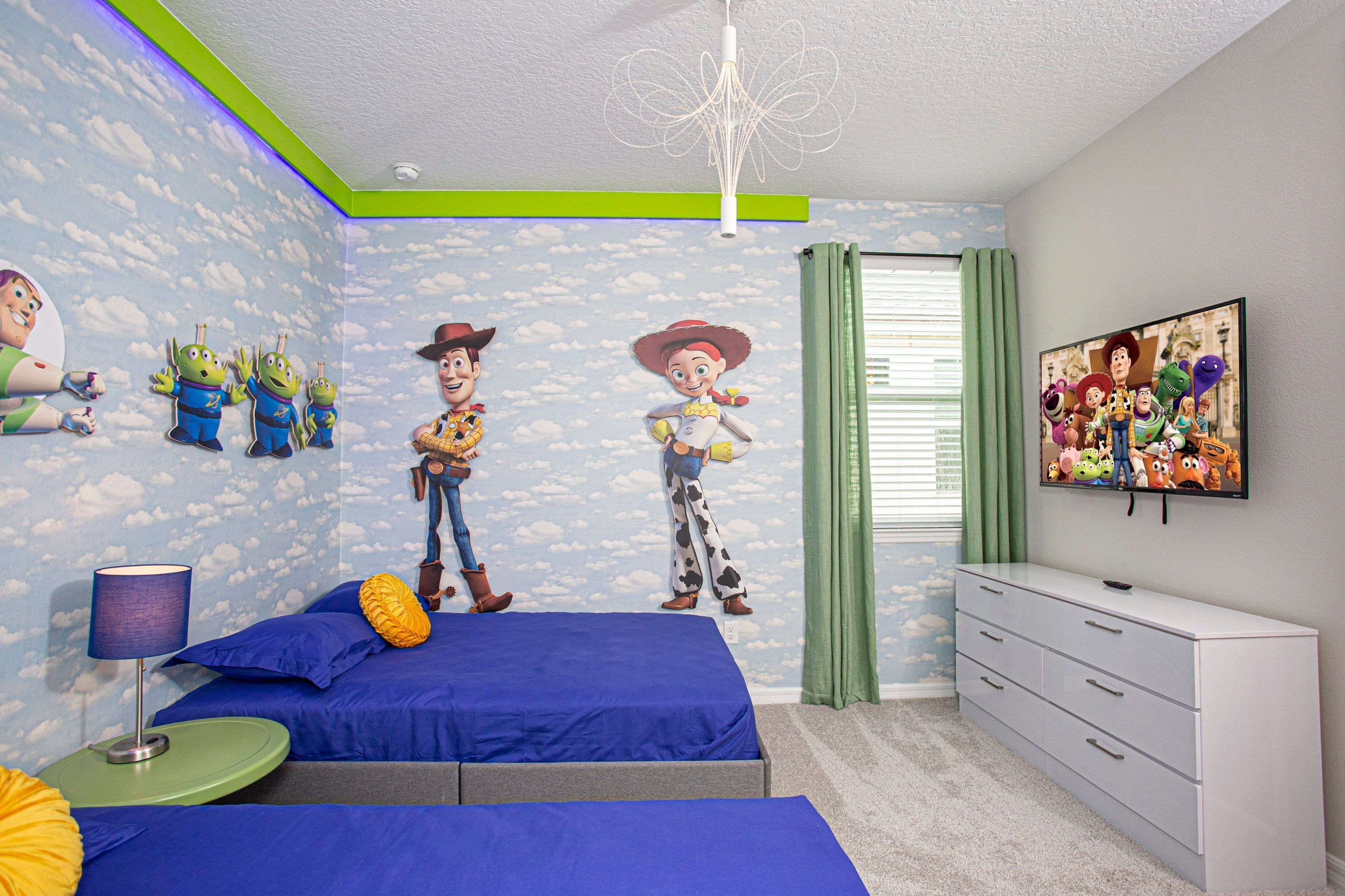 A bedroom with a bed, a dresser, a lamp, and a wall with a Woody and Buzz Lightyear mural.