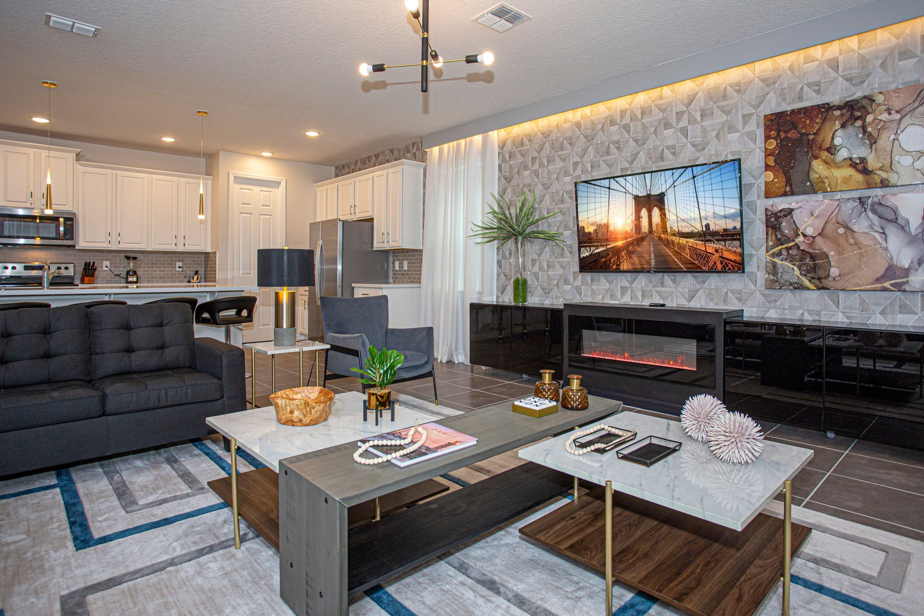 A modern living room with a sofa, coffee table, and fireplace. There is a kitchen in the background with white cabinets and appliances.