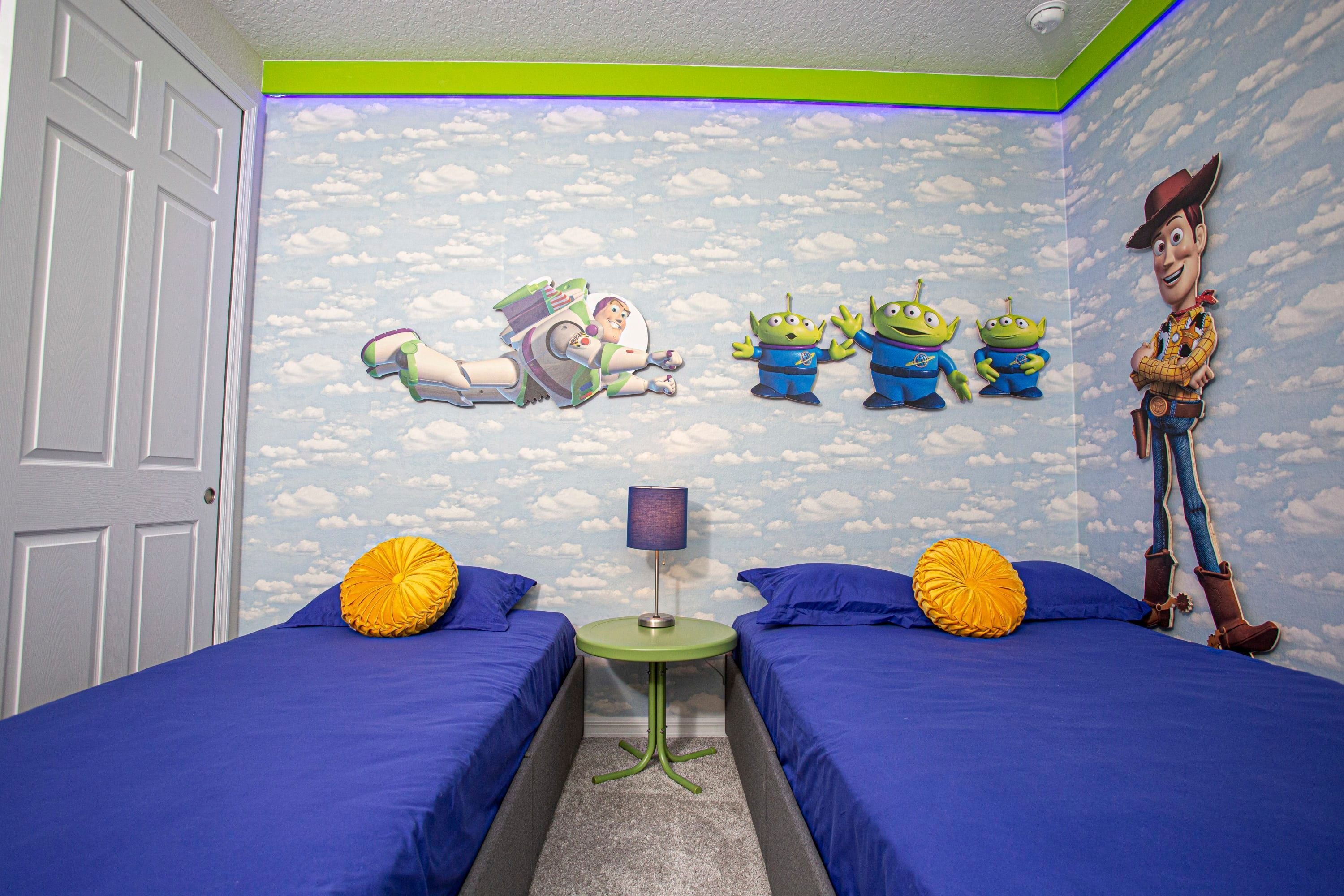 A bedroom with two beds, a nightstand, and a wall mural featuring characters from a space and cowboy-themed movie.