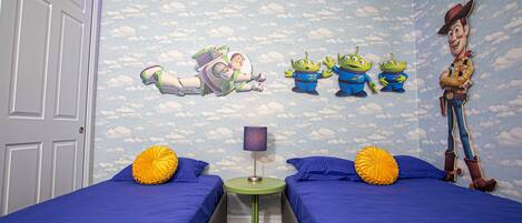 Un dormitorio con dos camas, una mesita de noche y un mural en la pared con personajes de una película de temática espacial y vaquera.