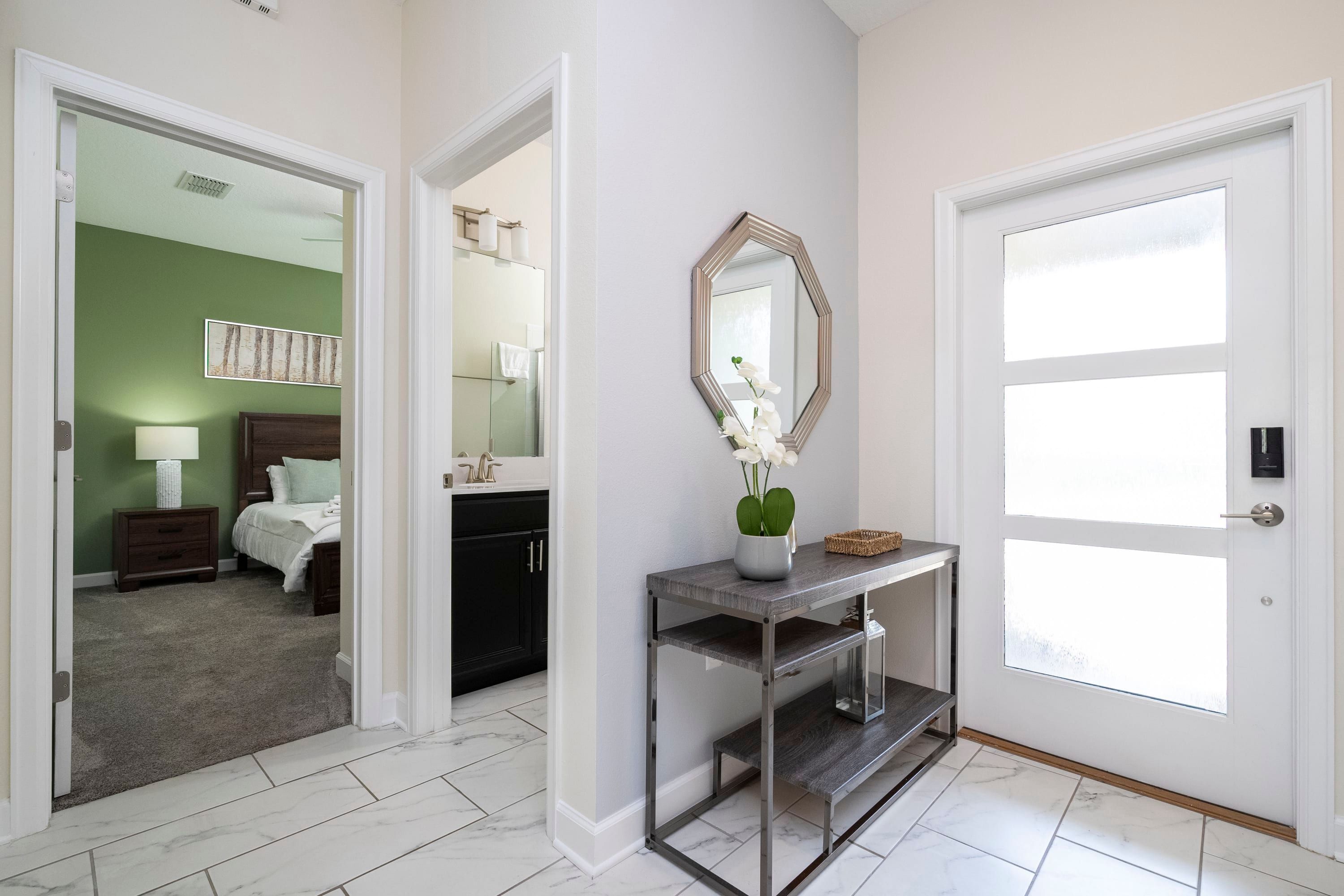 A hallway with a white door, a console table with a mirror, and a view into a bedroom with green walls and a nightstand.