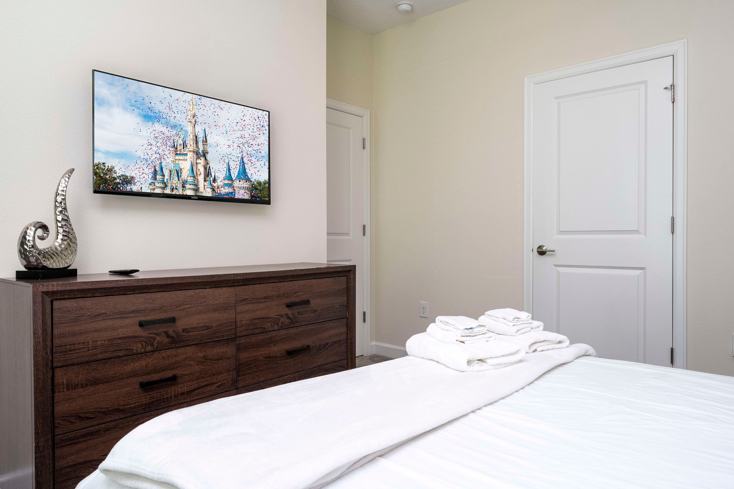 A hotel room with a bed, a dresser, a painting of a castle, and a door.