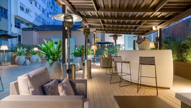 An outdoor patio area with a wooden ceiling, multiple tables and chairs, and potted plants.