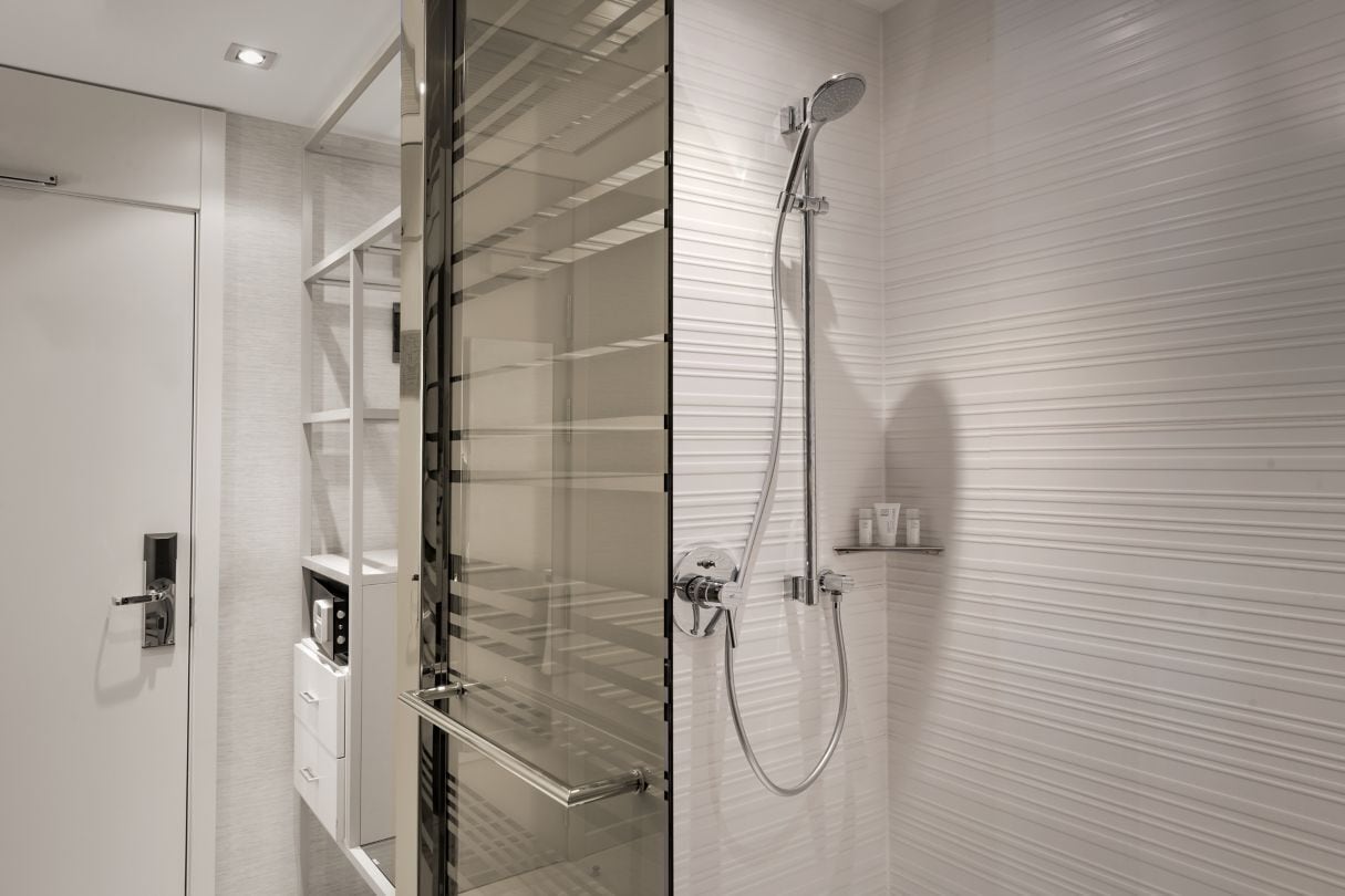 A modern bathroom with a glass shower enclosure, a built-in toilet, and a white tiled wall.
