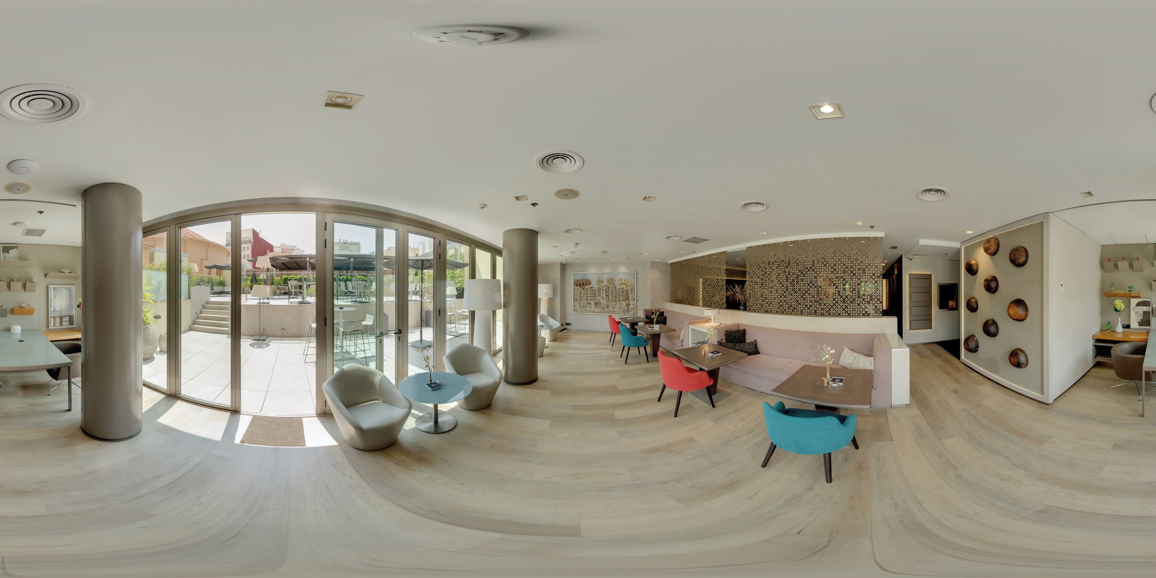 A modern hotel lobby with a curved floor design, large windows, and a reception area with a patterned wall.