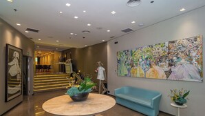 A lobby with a round table, a blue sofa, a large floral painting, and a staircase in the background.