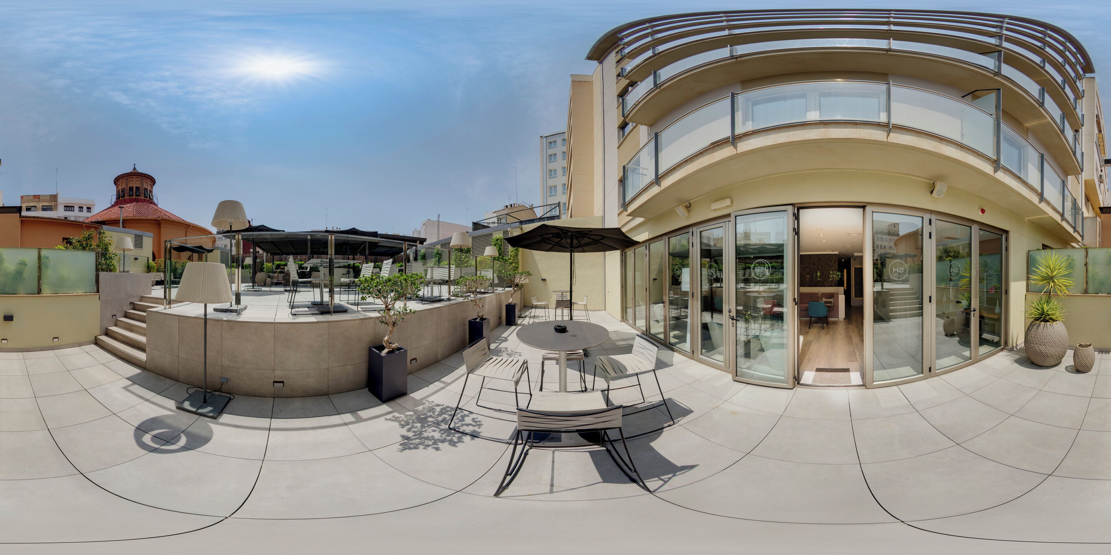 A modern building with a curved facade, a covered outdoor seating area with tables and chairs, and a glass entrance.