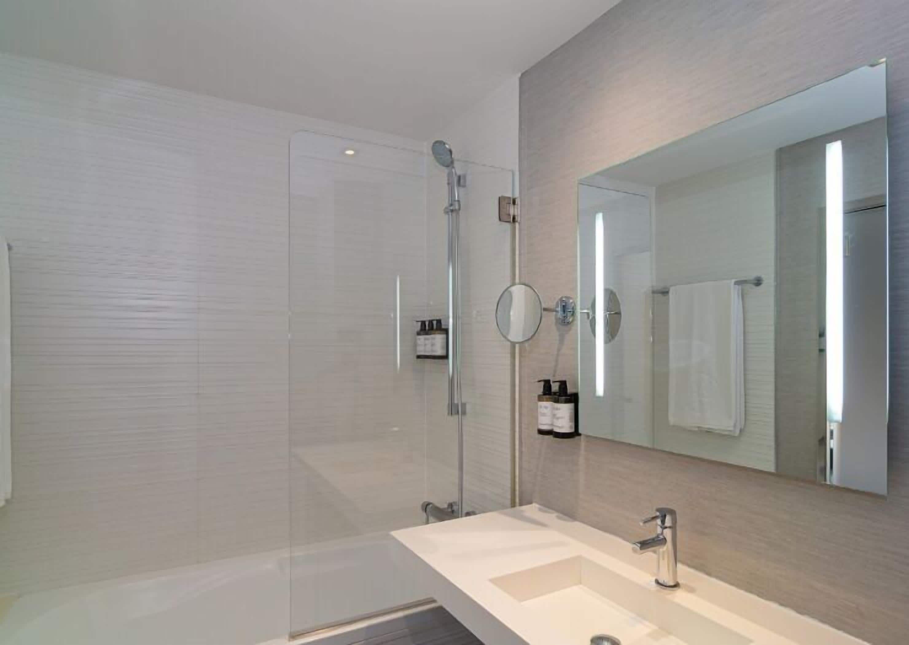 A modern bathroom with a glass shower enclosure, a large mirror, and a vanity with a sink.