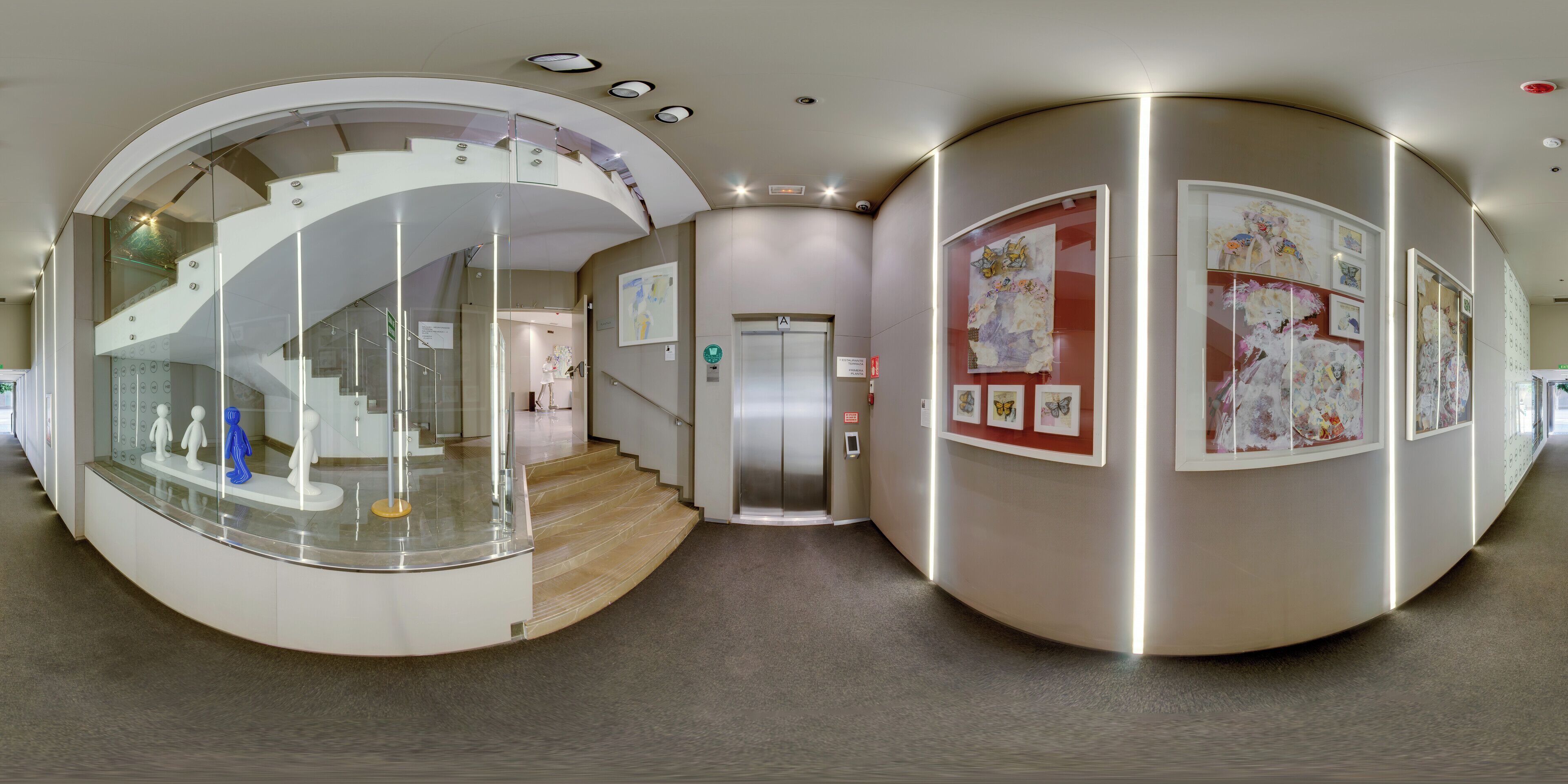 Un interior moderno con una escalera de cristal curva, un ascensor central y obras de arte en las paredes.