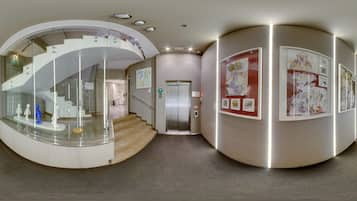 Un interior moderno con una escalera de cristal curva, un ascensor central y obras de arte en las paredes.