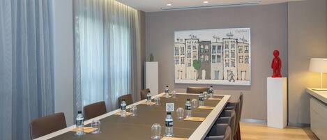 A modern conference room with a long table, chairs, water bottles, and a painting of buildings.