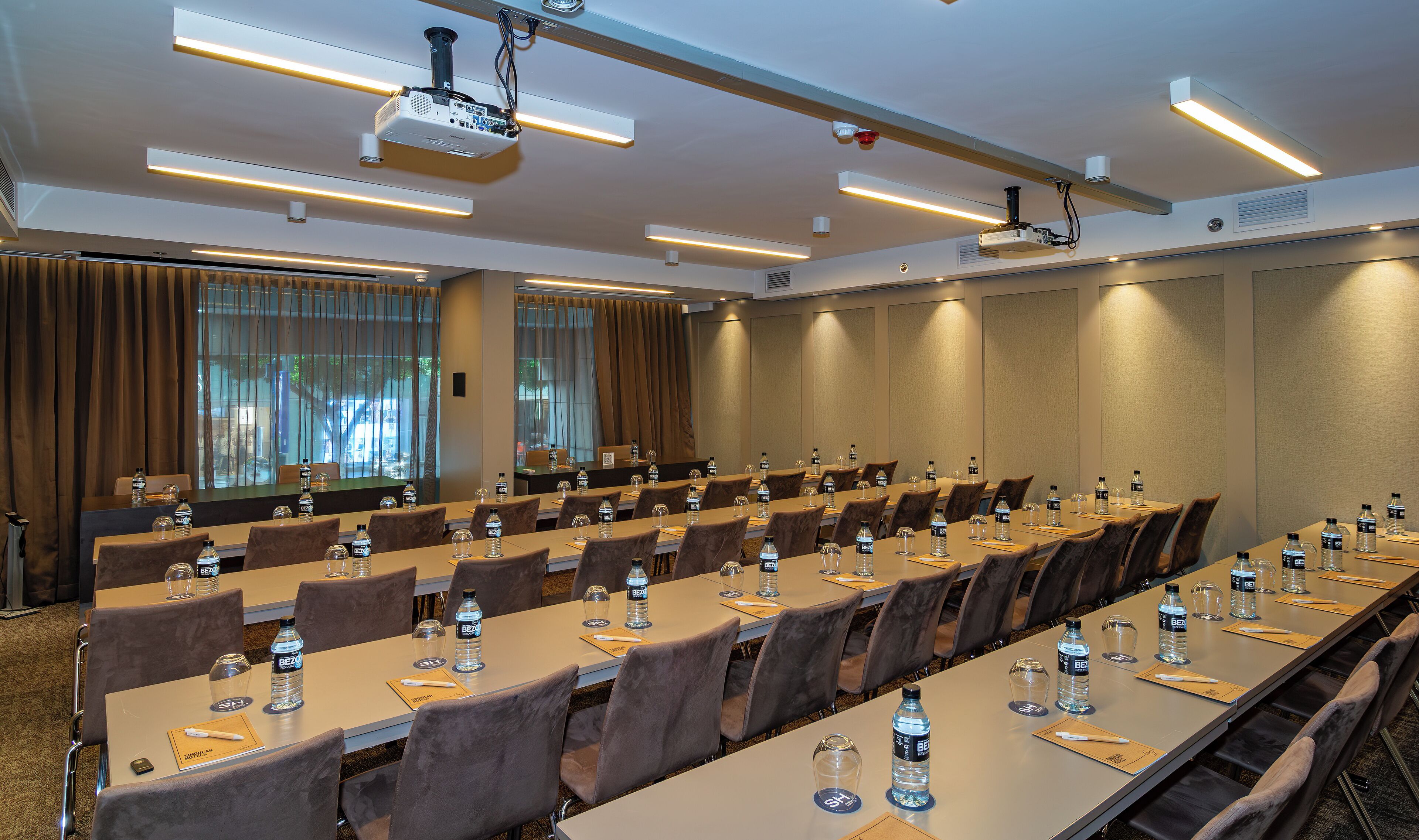Un salón de conferencias con mesas largas, sillas, botellas de agua y un proyector.