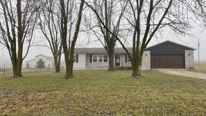 Une maison d’habitation avec un garage, entourée d’arbres et dotée d’une cour gazonnée.
