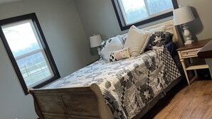 Une chambre à coucher avec un lit en bois, deux fenêtres, un ventilateur de plafond et une table de chevet avec une lampe.
