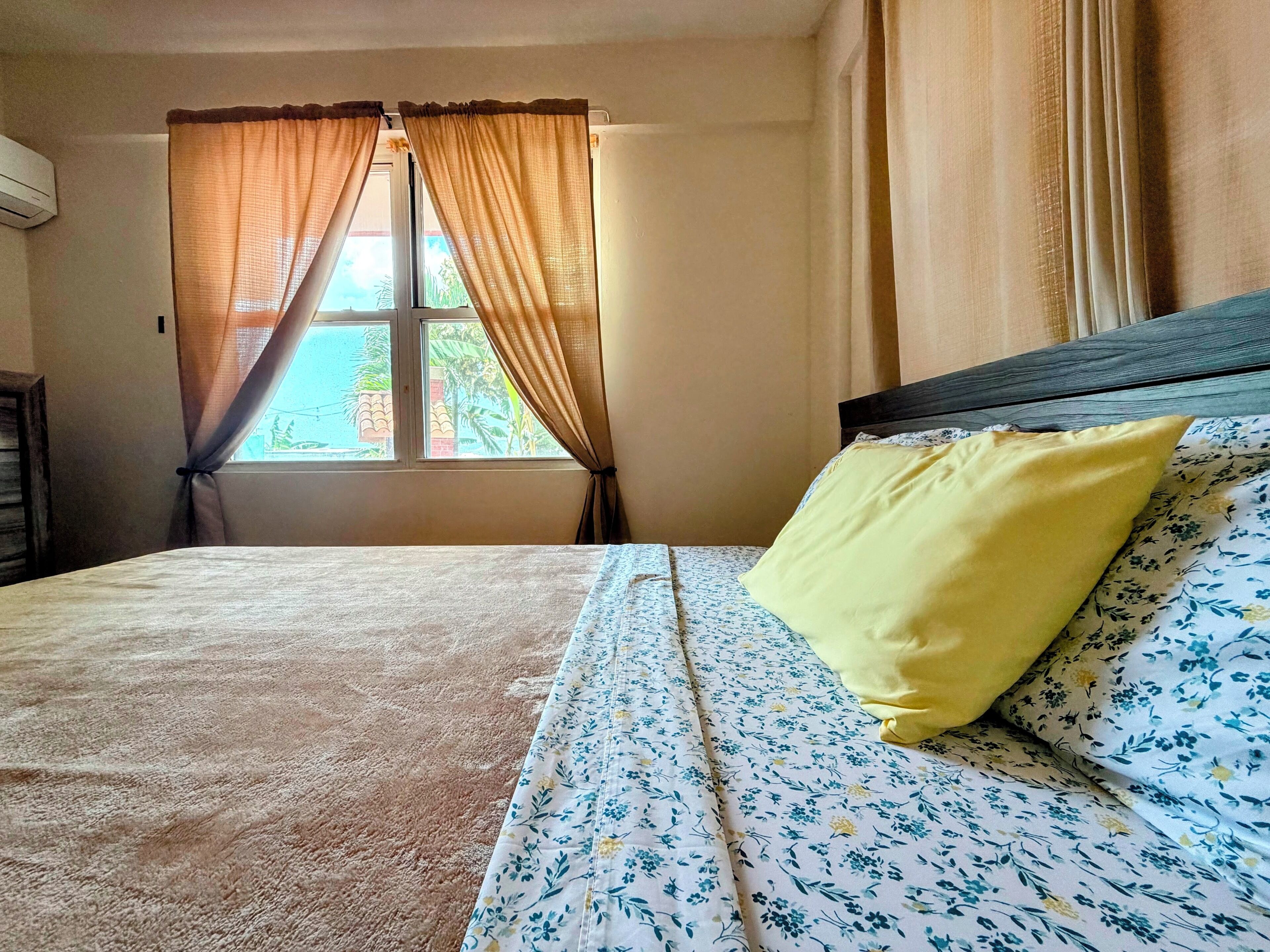 Bright, cozy bedroom with natural light, AC, and a spacious bed