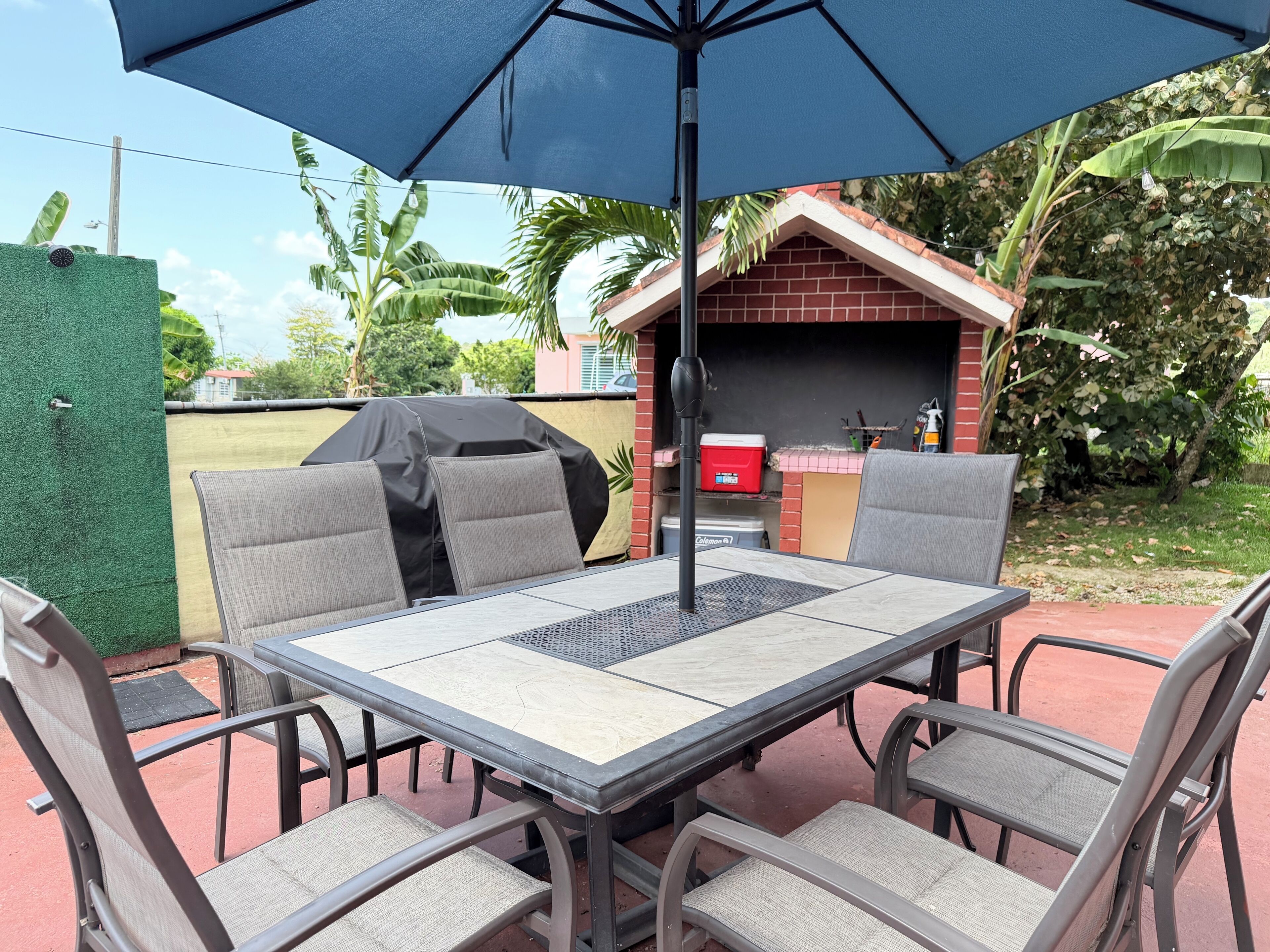 Un patio exterior con una mesa y sillas, una parrilla y una pequeña estructura de ladrillo.