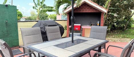 Un patio exterior con una mesa y sillas, una parrilla y una pequeña estructura de ladrillo.