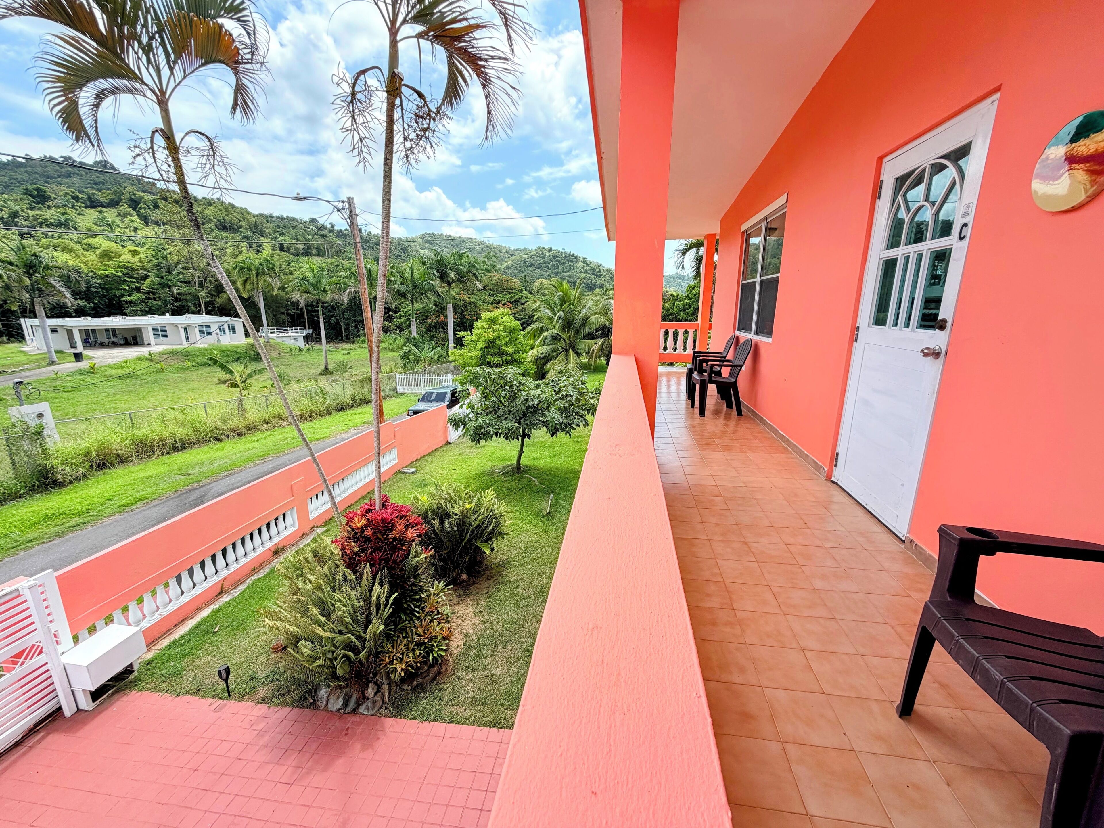 Un balcon donnant sur un paysage verdoyant, avec un bâtiment blanc en arrière-plan.
