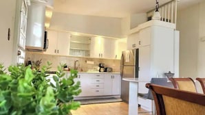 Una cuina moderna amb armaris blancs, un frigorífic d'acer inoxidable i una zona de menjador amb taula i cadires de fusta.
