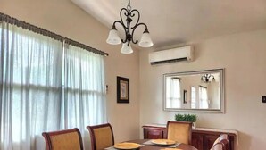 Una sala menjador amb taula de fusta preparada per a quatre, cadires, un lampadari, un aparell d'aire condicionat i un mirall a la paret.