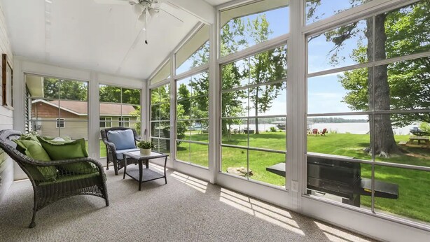 A sunroom with large windows, wicker furniture, and a ceiling fan. - Cozy Private Lakefront Cottage, Pet-Friendly with Private Dock (Kalkaska)