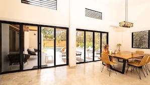 Amplia habitación con un gran ventanal corredero que da a un patio exterior. Se aprecia una mesa de comedor con sillas y una lámpara colgante.