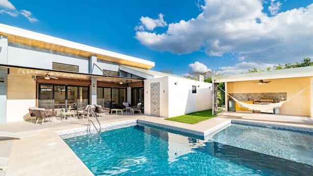 Un área de piscina moderna con cielo azul despejado, piscina y mobiliario exterior.