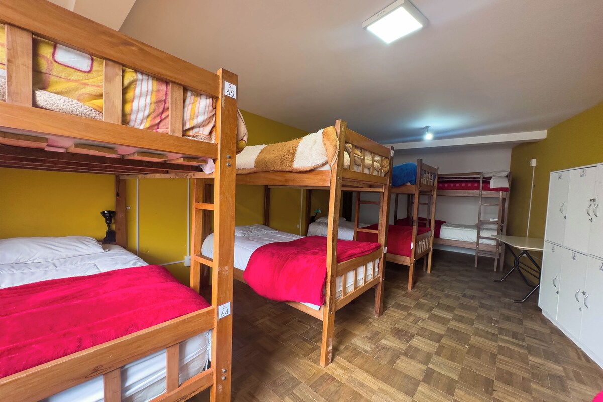 A dormitory room with bunk beds, wooden flooring, and a white wardrobe.