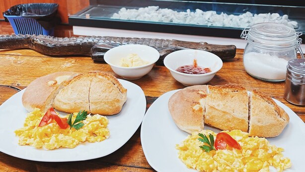A breakfast setup with two plates of scrambled eggs and toast, butter, jam, and a milk jug on a wooden table.