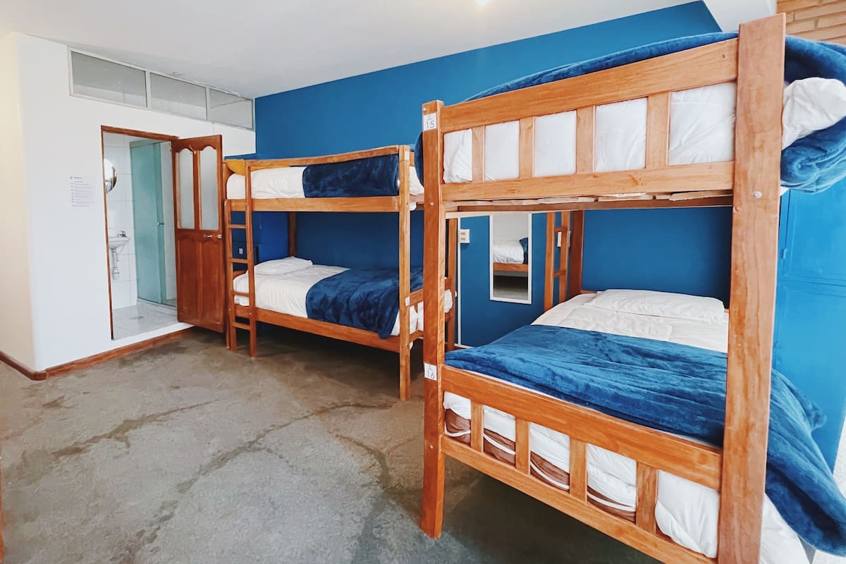 A dormitory room with bunk beds, a shower, and a door leading to a bathroom.