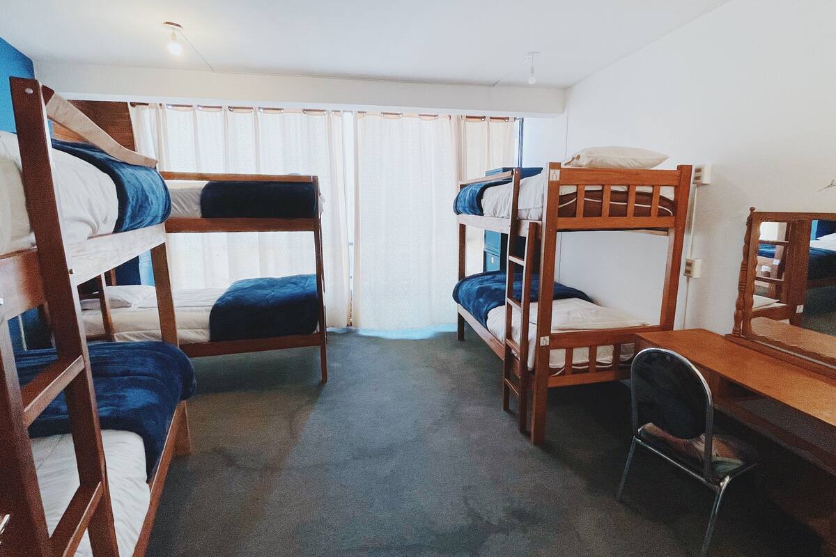 A dormitory room with bunk beds, a desk, and a chair.