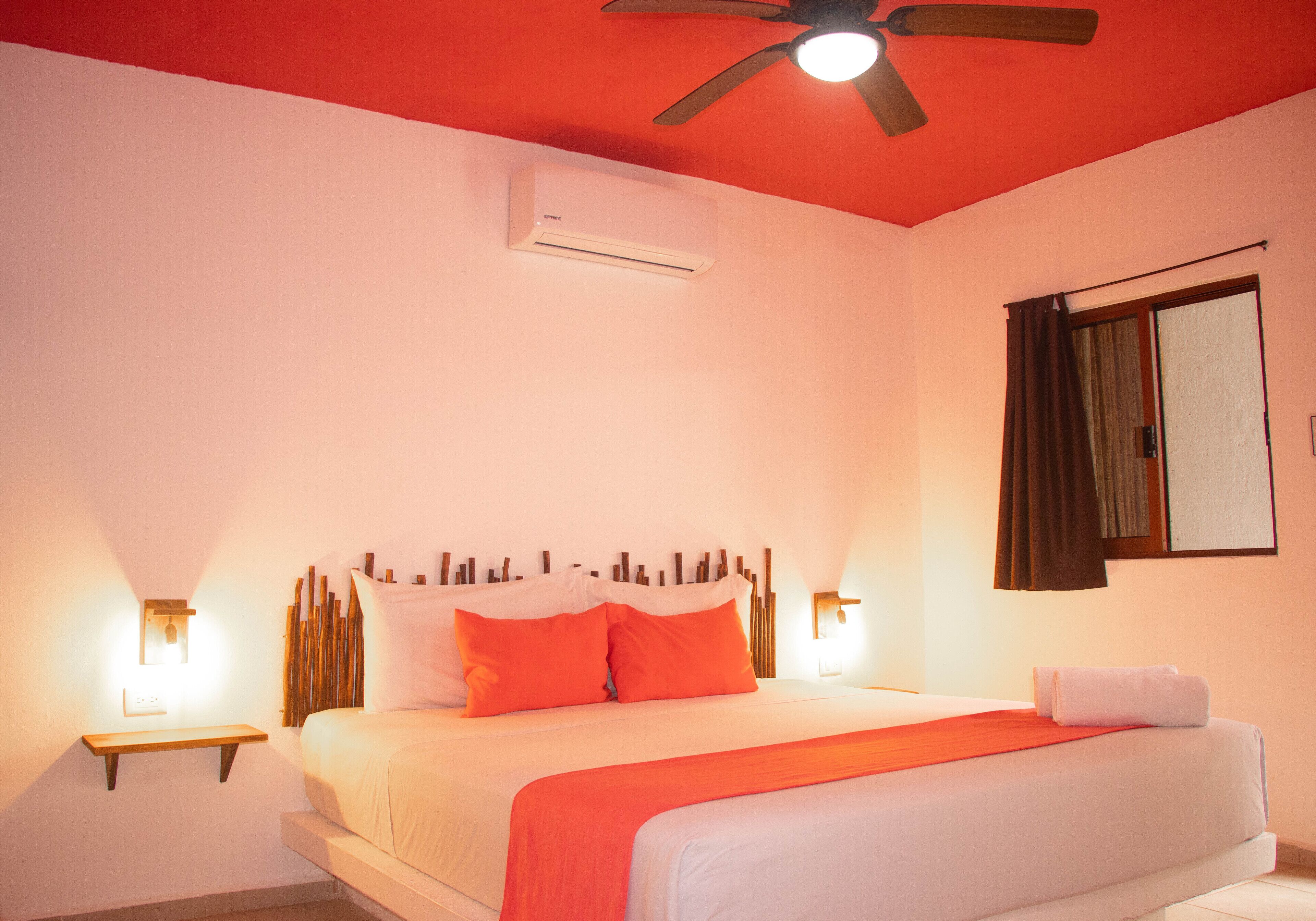 A bedroom with a bed, a ceiling fan, an air conditioning unit, and bedside lamps.