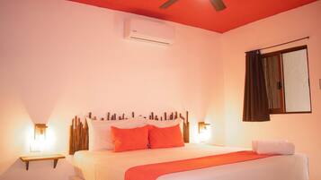 A bedroom with a bed, a ceiling fan, an air conditioning unit, and bedside lamps.