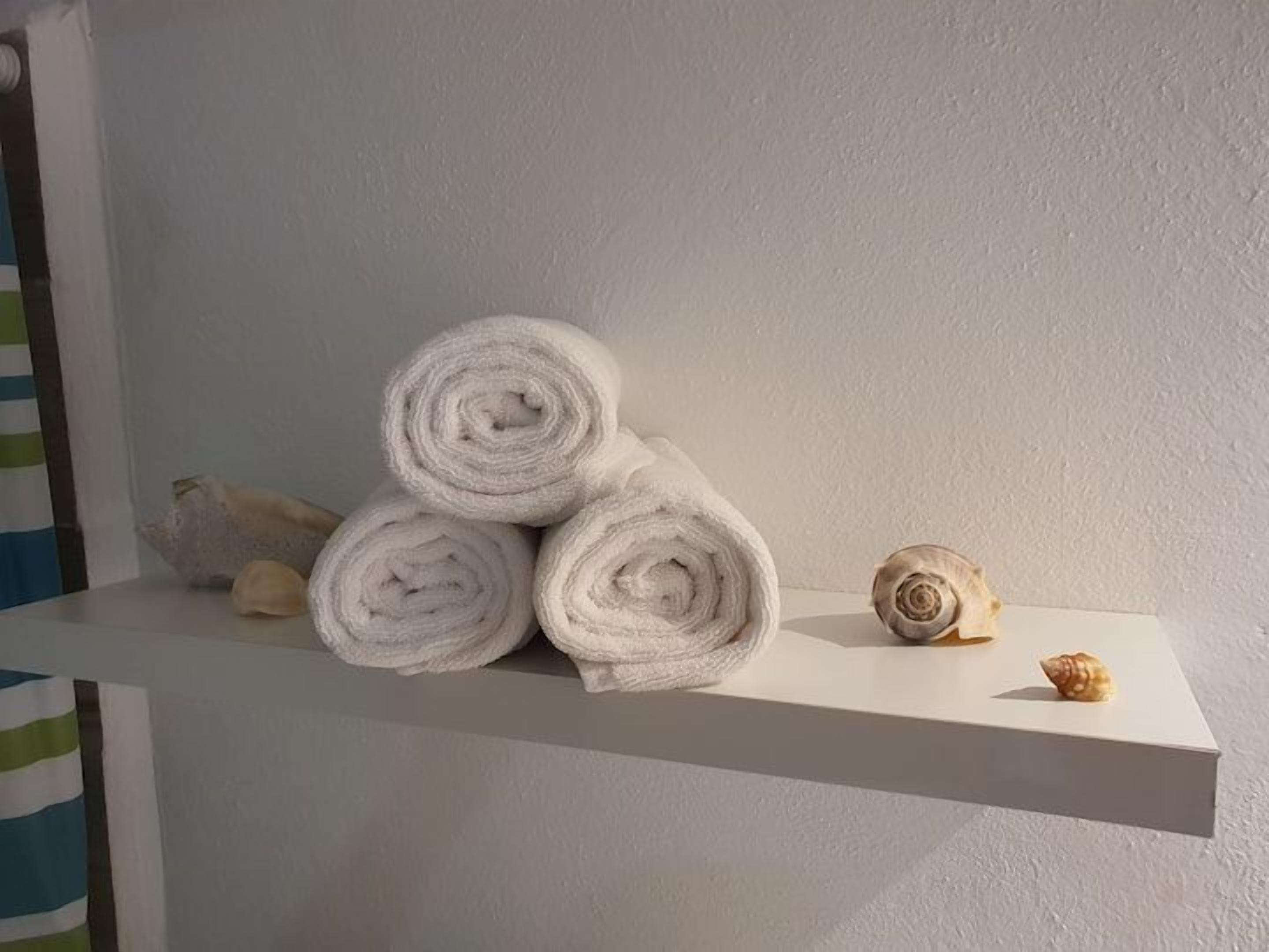 A white shelf with rolled white towels and two seashells.