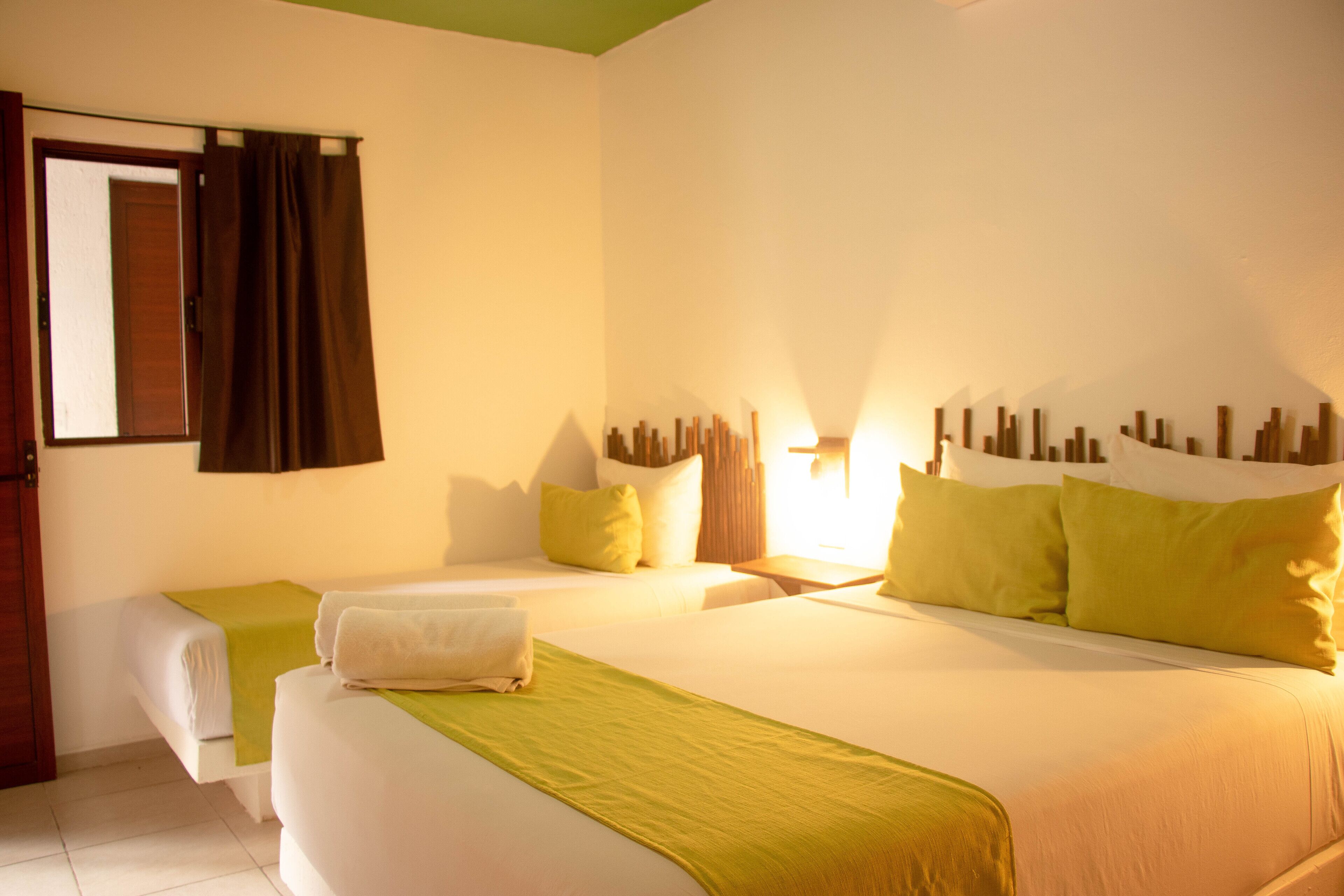 A hotel room with two beds, a green bed runner, and a wall-mounted light fixture.