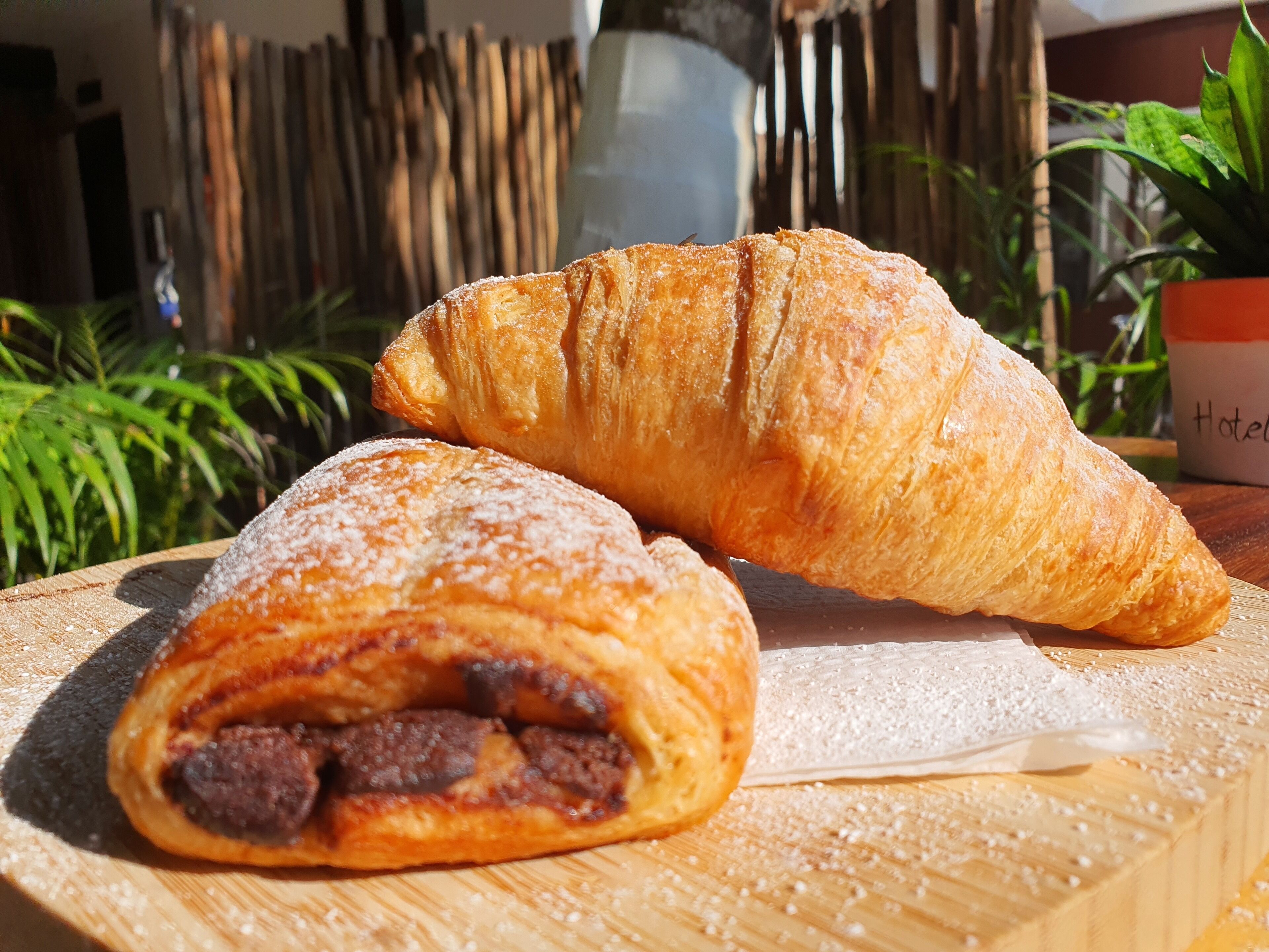 Un croissant y un pastel sobre una tabla de madera, con una planta y un letrero al fondo.