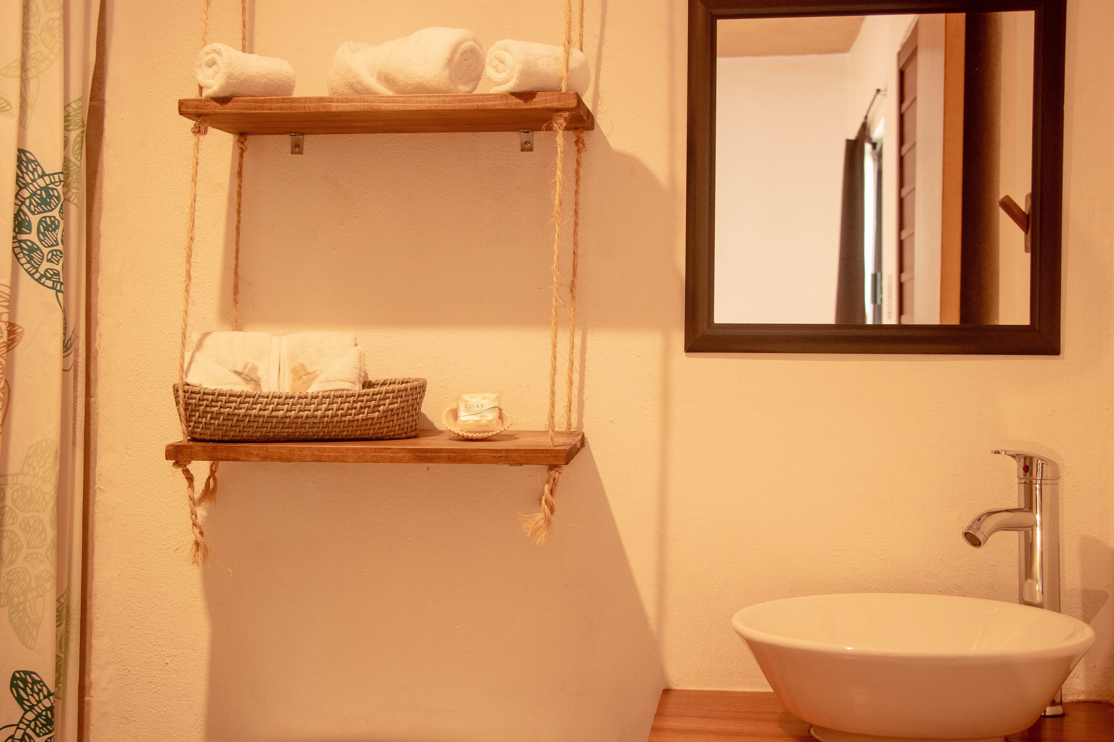A bathroom with a white sink, wooden shelves with towels, and a mirror.