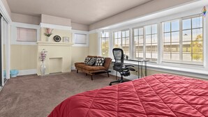 A bedroom with a large bed, a desk, a chair, a sofa, and a fireplace. - Spacious Home in the heart of the Bay (Oakland)