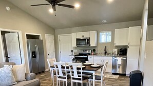 A modern kitchen with white cabinets, stainless steel appliances, and a dining area with a wooden table and chairs. - Cozy Sunset Retreat with a Beautiful Mountain View!  (Franklin)