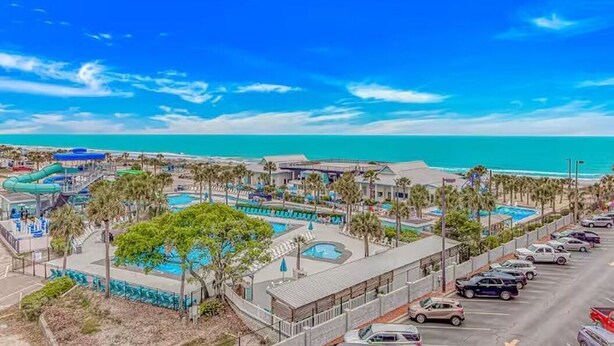 Ein Resort mit mehreren Schwimmbecken, einem Parkplatz und Meerblick.