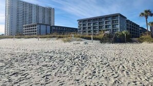 Ein Hotel direkt am Strand mit modernem Design, bestehend aus einem großzügigen Gebäude mit mehreren Balkonen und einem separaten Bauwerk mit einer Treppe zum Strand.