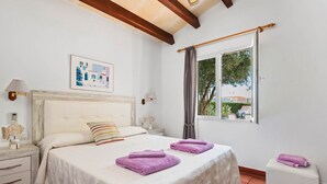 Une chambre à coucher bien aménagée, avec un grand lit, deux tables de chevet, une fenêtre avec des rideaux et une vue sur la verdure à l’extérieur.