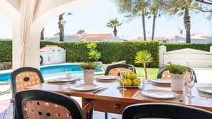 Un espace de restauration en plein air avec vue sur une piscine, des tables et des chaises disposées avec soin, et des plantes en pot.