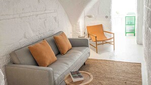 A cozy living room with a grey sofa, two brown cushions, a round wooden side table with a book, a floor lamp, and a green chair. - Pere Alcantara 40, 3 bedroom house, Ciutadella (Ciutadella de Menorca)