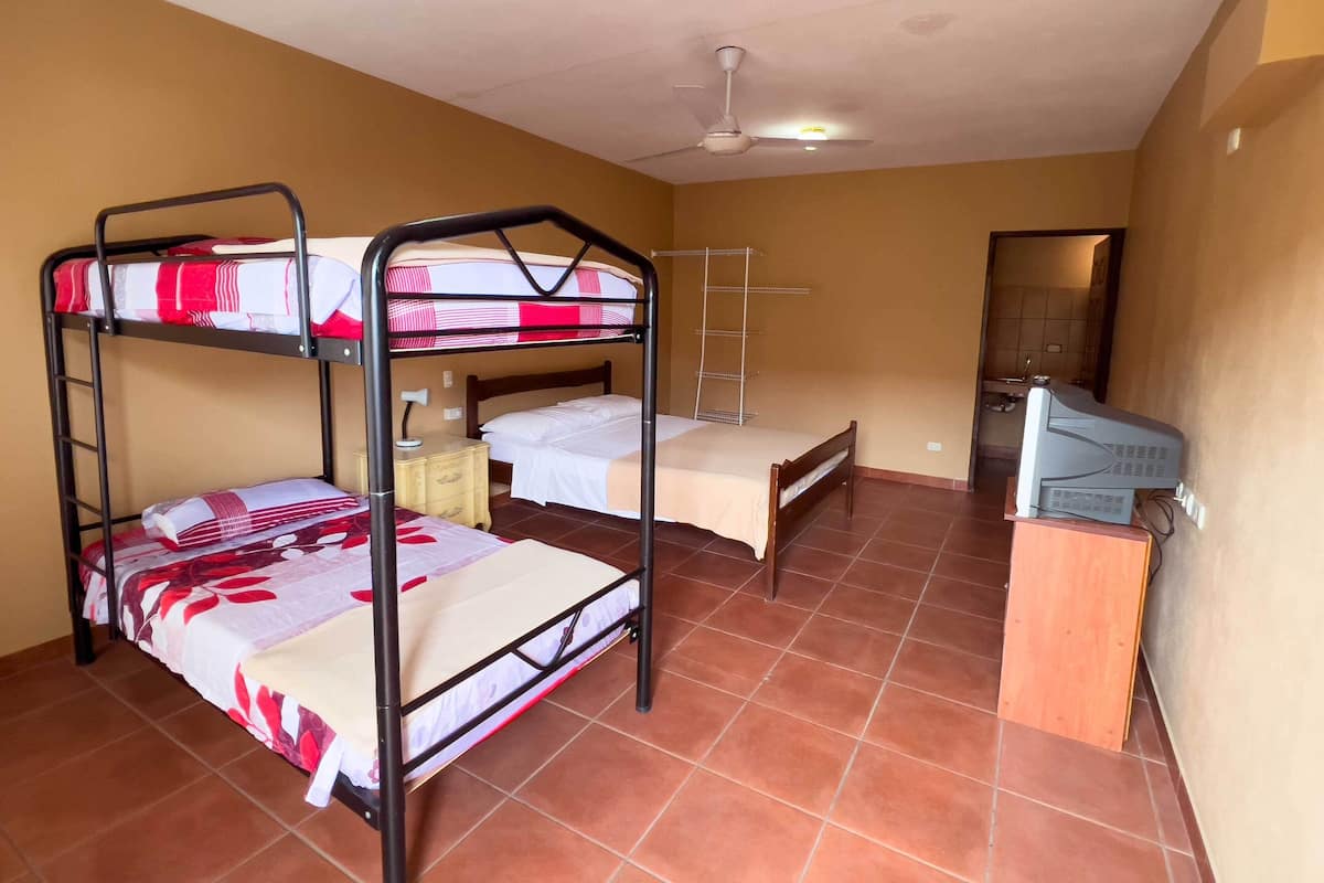 A dormitory room with bunk beds, a desk, a chair, a lamp, and a ceiling fan.